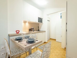 Een kleine keuken met een magnetron, koffiezetapparaat en een eethoekje met een tafel voor twee personen.