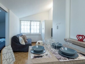 A modern, well-lit room with a dining area set for four, a sofa, and a large window with heart-shaped decorations. - Beautiful apartment for 3 people with WIFI and TV (Madesimo)