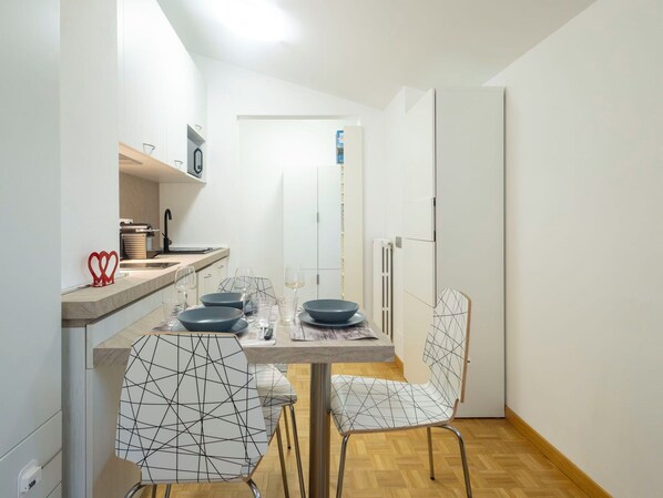 Een kleine keuken met een eettafel, stoelen en een koelkast.