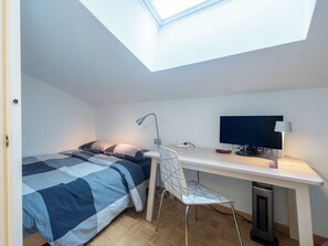 Een kleine kamer met een bed, een bureau, een stoel, een televisie en een dakraam.