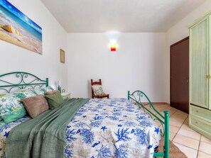 Ein Schlafzimmer mit einem Bett, einem Sessel, einem Nachttisch, einer Lampe, einem Gemälde und einem Kleiderschrank.