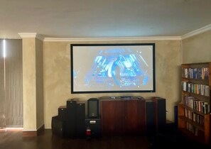 A home theater setup with a large screen, speakers, and a bookshelf. - Private Pretoria Villa for 12 with Pool, Cinema, Bar & Firepit (Pretoria)
