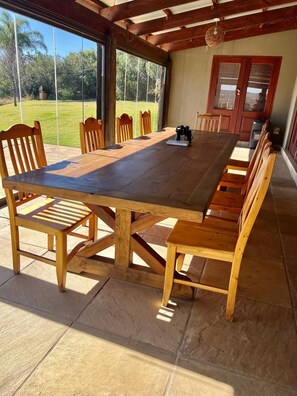 A wooden dining table with benches, a large window, and a door. - Private Pretoria Villa for 12 with Pool, Cinema, Bar & Firepit (Pretoria)