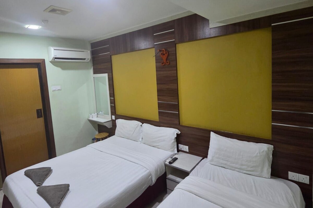 A hotel room with two beds, a wooden headboard, an air conditioning unit, a bedside table, and a nightstand.