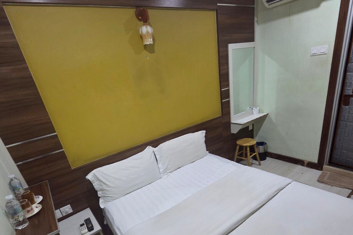 A hotel room with a bed, a bedside table with a phone, a mirror, and a small stool.