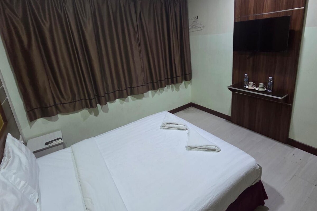 A hotel room with a bed, a TV mounted on a wooden cabinet, and a small shelf with toiletries.
