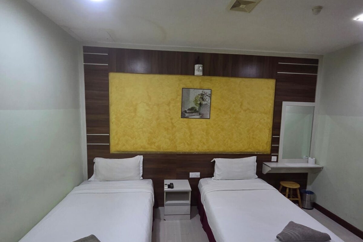 A hotel room with two single beds, a small bedside table with a lamp, a mirror, and a wall-mounted picture.