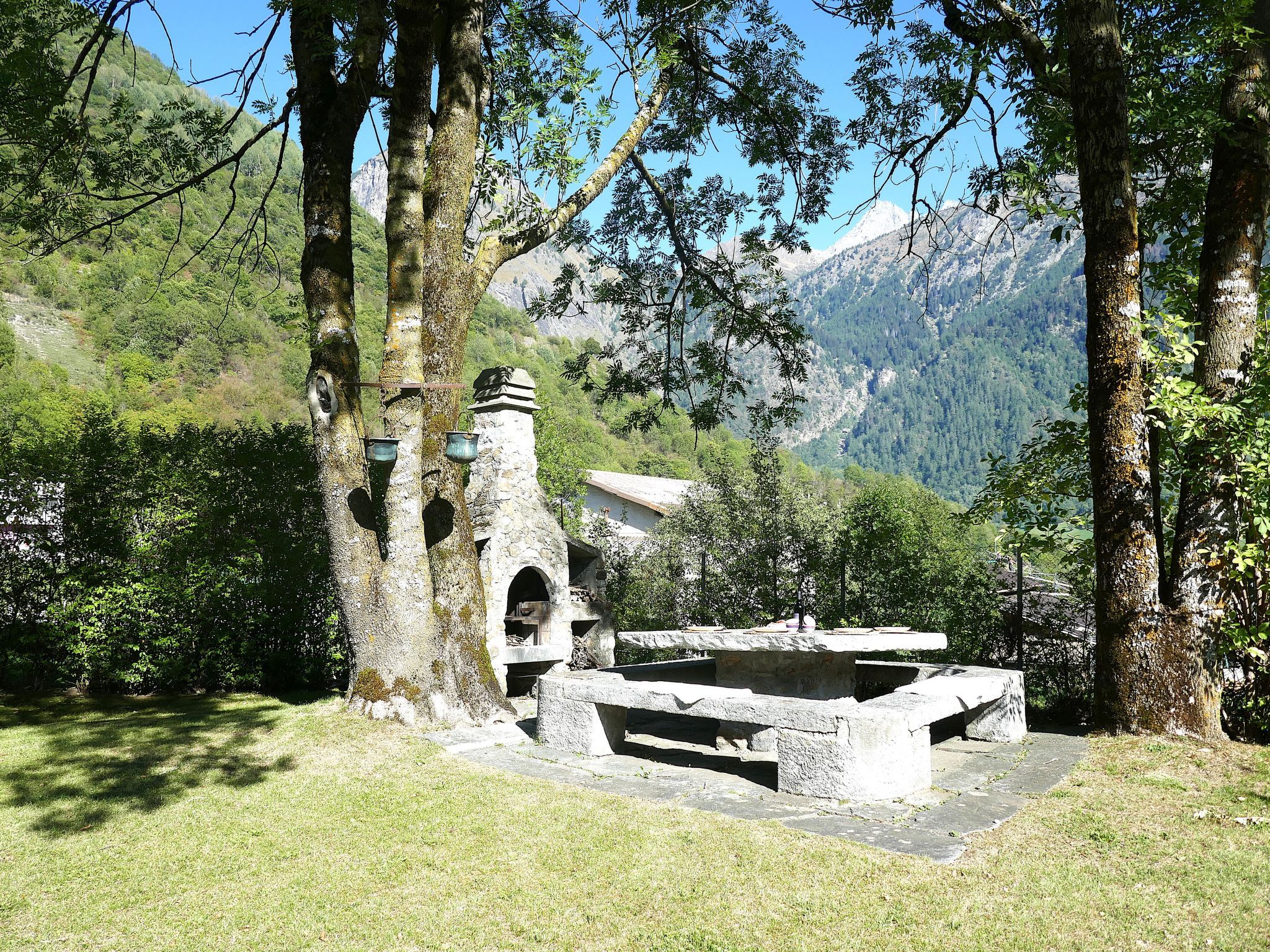 A stone structure with a bench and a small building, surrounded by trees and mountains.