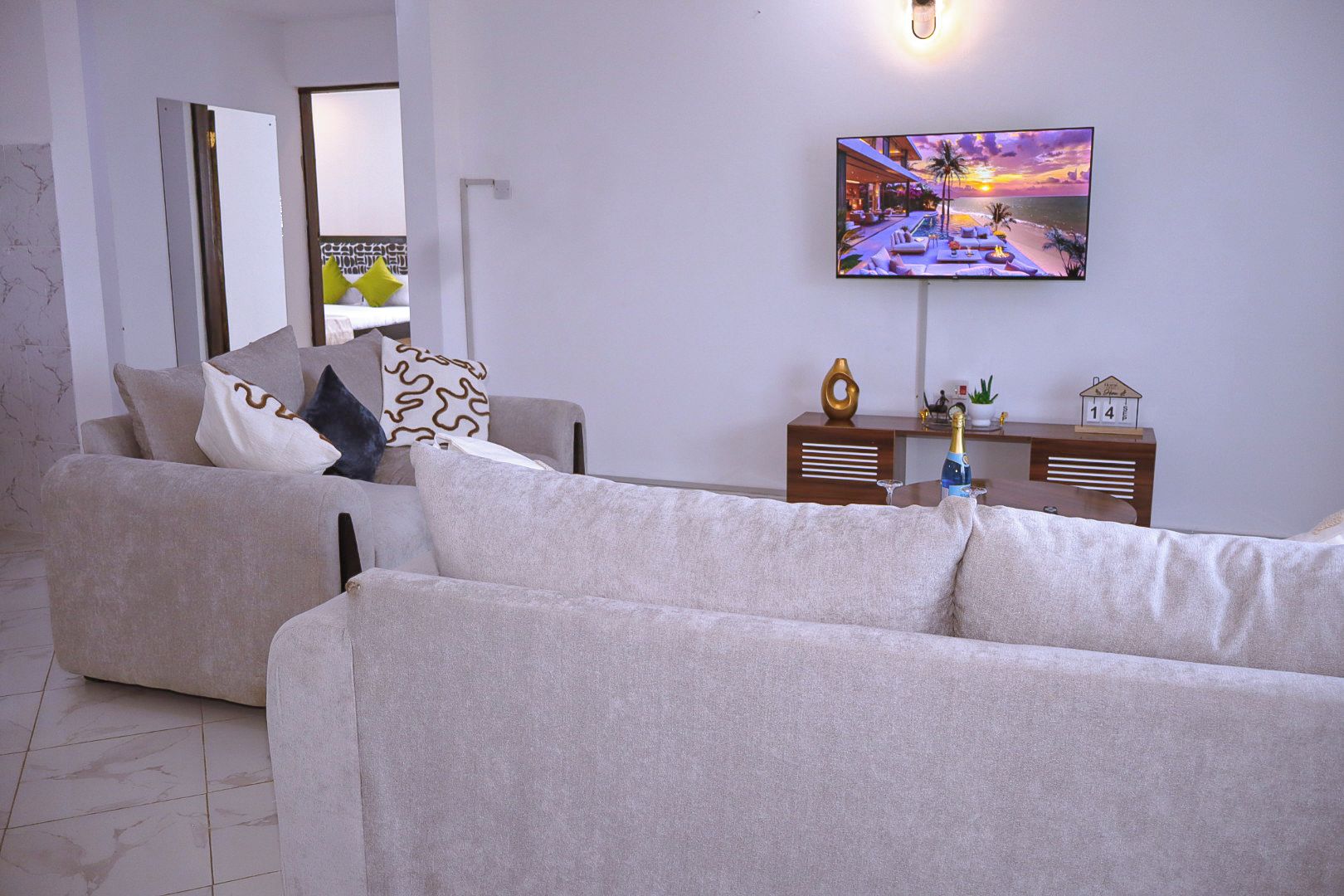 A modern living room with a sofa, a television mounted on the wall, and a small table with a bottle and a decorative item.