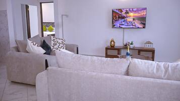 A modern living room with a sofa, a television mounted on the wall, and a small table with a bottle and a decorative item.
