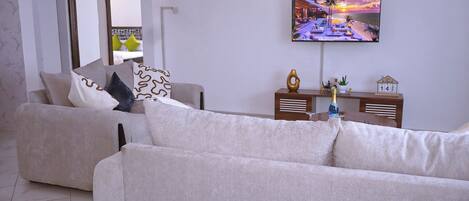 A modern living room with a sofa, a television mounted on the wall, and a small table with a bottle and a decorative item.
