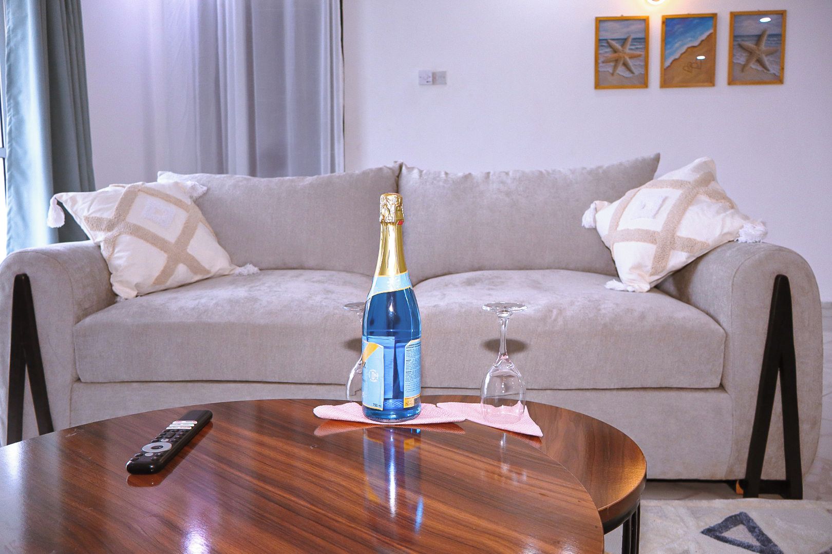 Ein Wohnzimmer mit einer Couch, einer Fernbedienung, einer Champagnerflasche und einem Weinglas auf einem Holztisch.