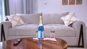 Ein Wohnzimmer mit einer Couch, einer Fernbedienung, einer Champagnerflasche und einem Weinglas auf einem Holztisch.