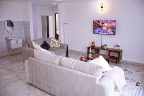 A modern living room with a sofa, a television, and a decorative wall piece. - 2 BEDROOM APARTMENT IN DIANI, UPTO 6 GUESTS C, 5 MINS DRIVE TO THE BEACH (Diani Beach)