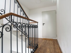 A staircase with a wooden handrail and black metal balusters, leading to a white door with a doormat. - Villa Acquarossa 1736 by Interhome (Acquarossa)