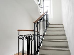 A staircase with a wooden handrail and black wrought iron balusters. - Villa Acquarossa 1736 by Interhome (Acquarossa)