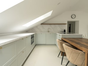 A modern kitchen with a skylight, white cabinets, a wooden dining table, and two chairs. - Villa Acquarossa 1736 by Interhome (Acquarossa)