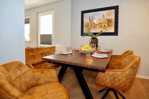A dining area with a wooden table, four upholstered chairs, and a framed painting on the wall. - New designer apartment with a terrace in the Old Town (Nordhausen)