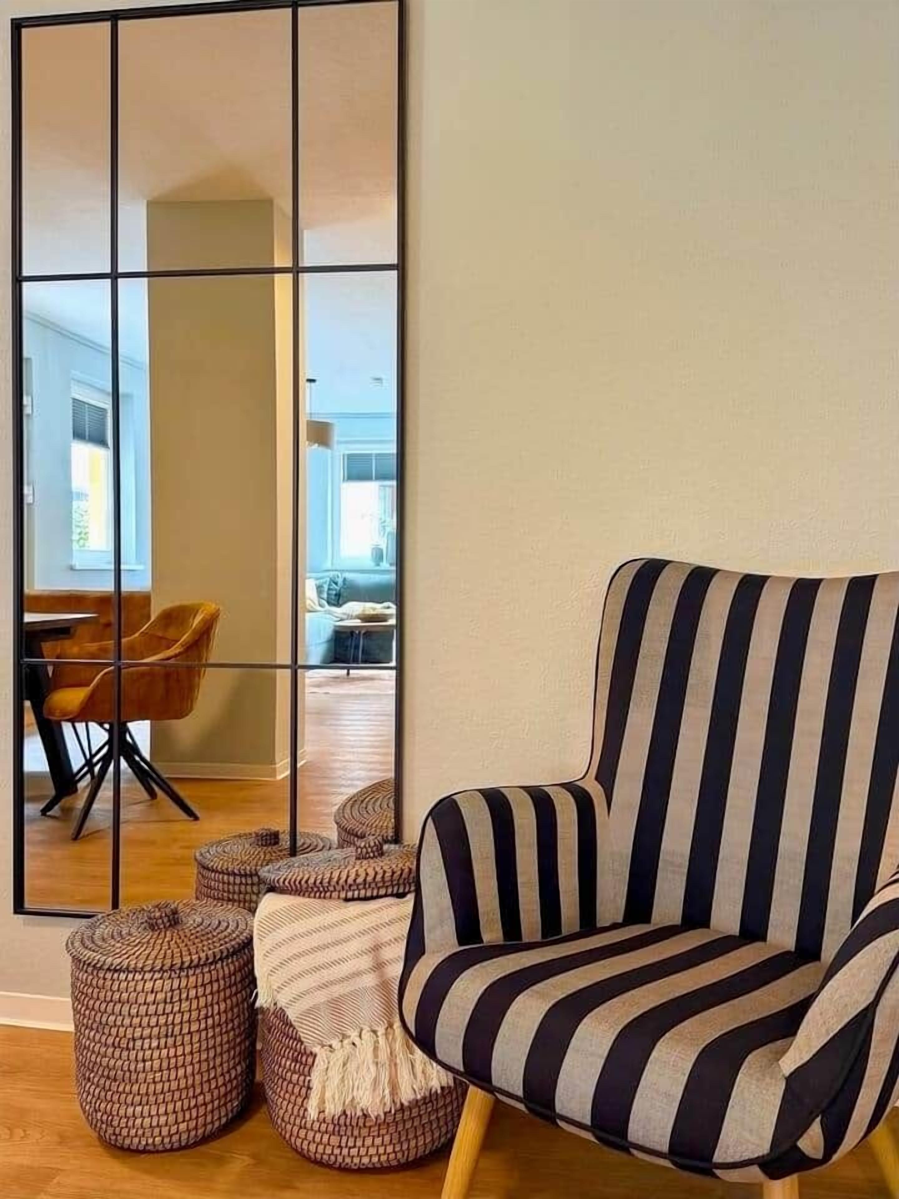 Een kamer met een gestreept fauteuil, een grote spiegel en twee voetenbankjes.