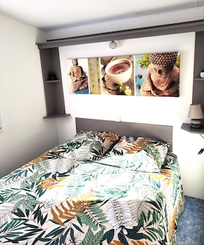 Une chambre avec un lit, une étagère fixée au mur sur laquelle se trouve une statue de Bouddha, et un mur orné d’une statue de Bouddha et d’un bol.