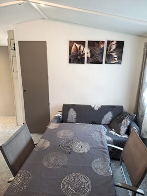 Une pièce comprenant un canapé, une table à manger recouverte d’une nappe à motifs et trois tableaux accrochés au mur.