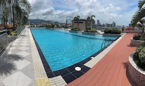 Una piscina con vistas a la ciudad, rodeada por una terraza con baldosas y palmeras.