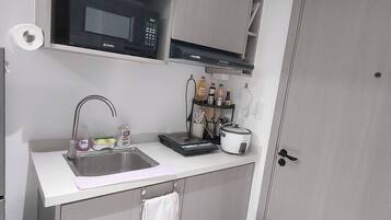 Una cocina compacta con microondas, lavabo y una pequeña zona de encimera con diversos objetos.