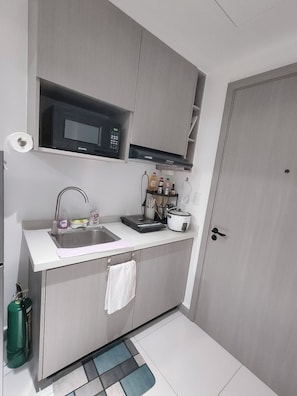 Una cocina compacta con microondas, lavabo y una pequeña zona de encimera con diversos objetos.