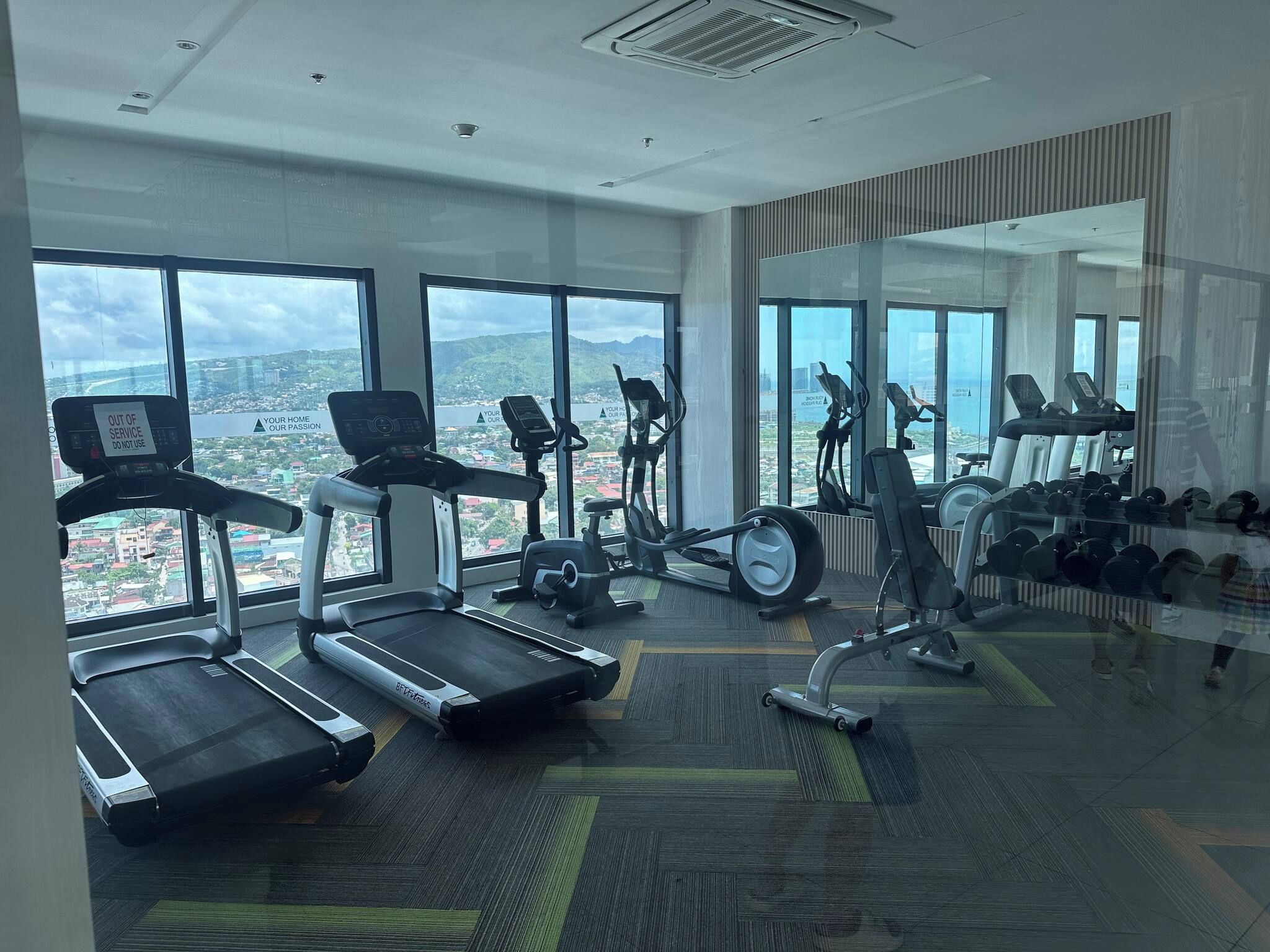 Une salle de sport équipée de tapis de course, de vélos d’appartement et d’un mur recouvert de miroirs.