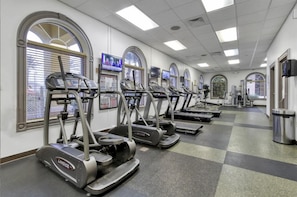 A gym with multiple Landice treadmills arranged in a row, large windows with blinds, and a checkered floor pattern. - The Regal Escape W/ Lazy River | Near Disney (Davenport)