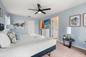 Une chambre à coucher avec un lit, un ventilateur de plafond, une télévision et des œuvres d’art accrochées aux murs.