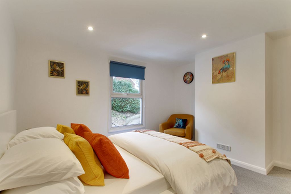 A bedroom with a bed, pillows, a chair, a window, and artwork on the walls.