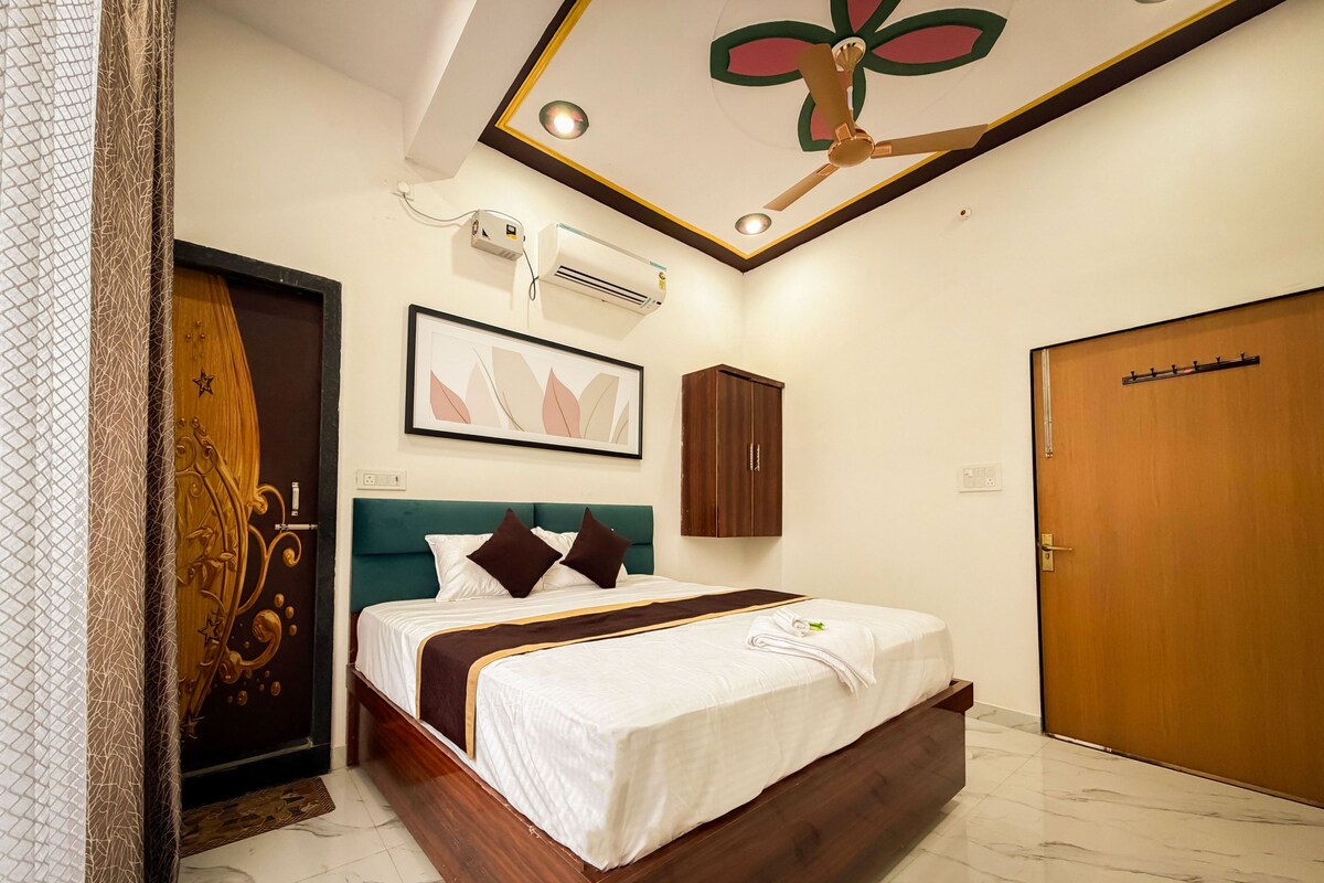 A hotel room with a bed, a ceiling fan, an air conditioning unit, a wooden wardrobe, and a door.