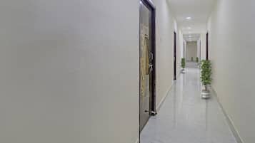 Un pasillo con puertas a ambos lados, suelo de baldosas y macetas a lo largo de la pared derecha.