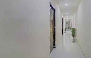A corridor with doors on both sides, a tiled floor, and potted plants along the right wall.