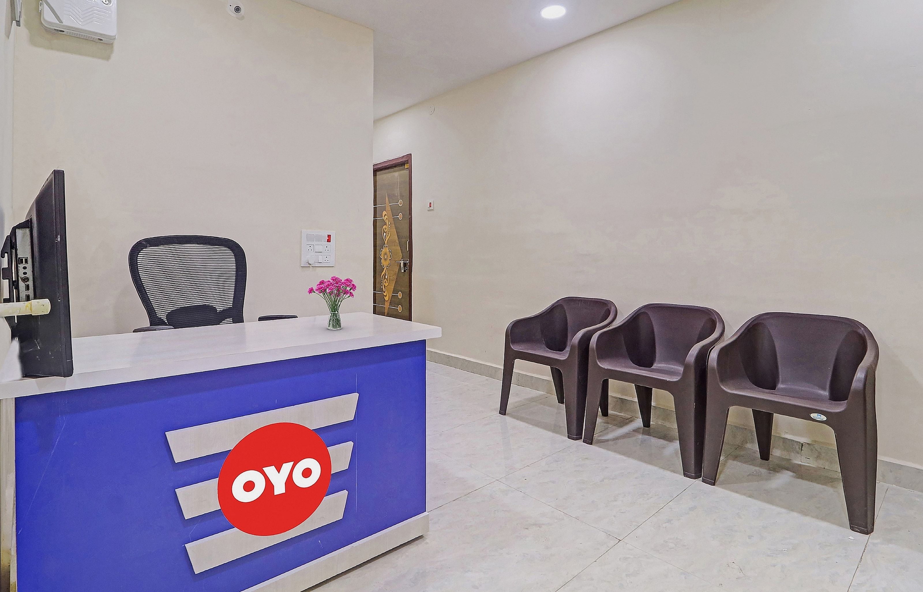 A reception area with a blue counter, a black chair, and three plastic chairs.
