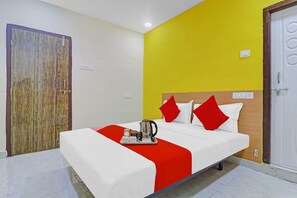 Habitación de hotel con una cama, un plaid rojo, una cafetera y un cabecero de madera.