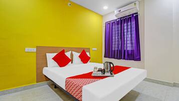 Quarto de hotel com cama, colcha vermelha e branca, bandeja com chaleira e janela com cortinas roxas.