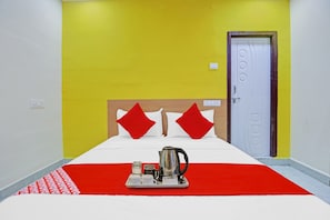 A hotel room with a bed, a tray with a kettle and cups, and a door with a circular handle.