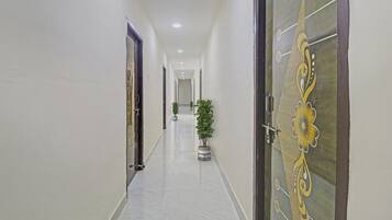 Corredor com portas em ambos os lados, um vaso de planta ao centro e teto com iluminação embutida.