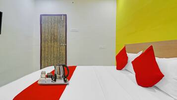 Quarto de hotel com uma cama, um tabuleiro com chaleira e um edredom vermelho e branco.