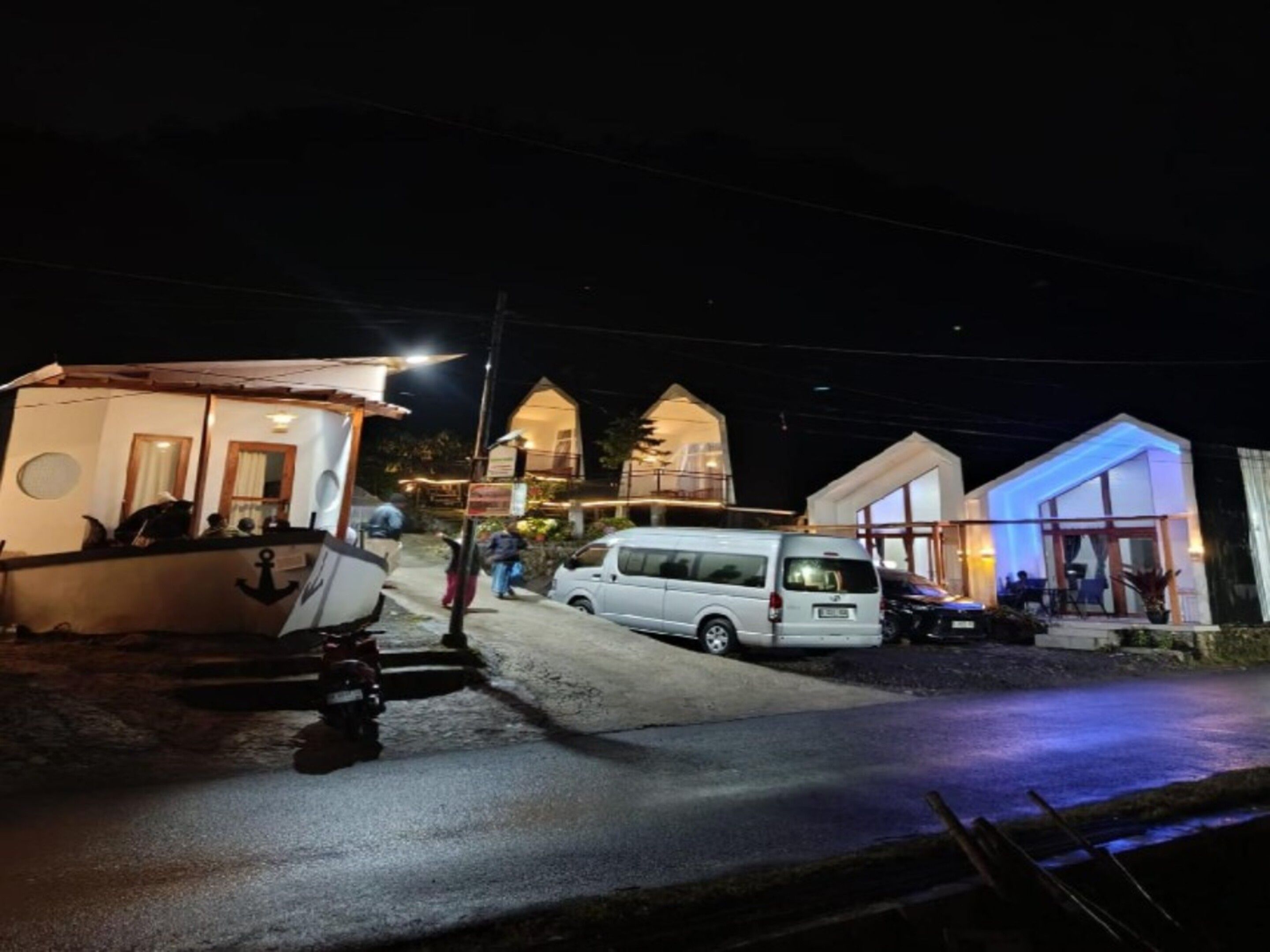Une propriété située sur la côte, avec un bateau amarré à proximité, un fourgon blanc garé dans la rue et un bâtiment doté d’une façade en verre.