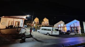 Une propriété située sur la côte, avec un bateau amarré à proximité, un fourgon blanc garé dans la rue et un bâtiment doté d’une façade en verre.