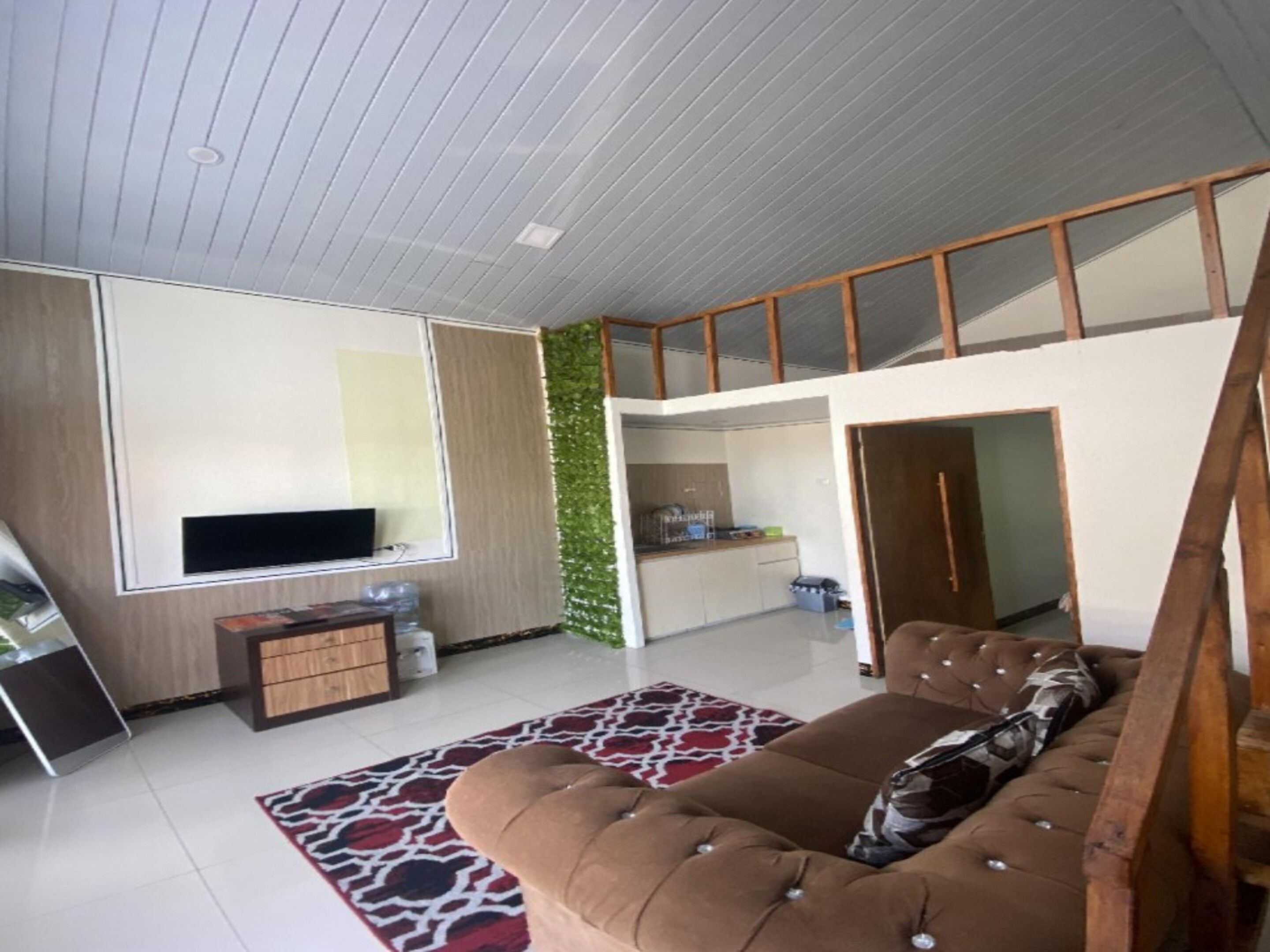 A modern living room with a sofa, a flat-screen TV, and a kitchen area visible through an open door.
