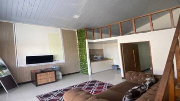 A modern living room with a sofa, a flat-screen TV, and a kitchen area visible through an open door.