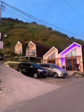 Un edificio residencial con techo inclinado, balcón y entrada con coches aparcados.