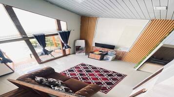 En moderne stue med sofa, sofabord og tv-møbel. Der er et stort vindue med gardiner, udsigt til det fri og en mønstret måtte på gulvet.