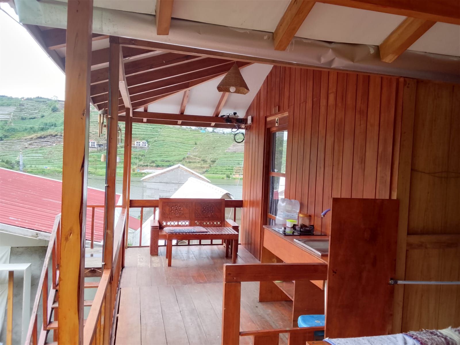 Ein Holzbalkon mit einer Bank und einem Tisch, der auf ein Gebäude mit rotem Dach und eine grüne Landschaft blickt.