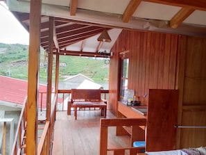 Un balcón de madera con un banco y una mesa, con vistas a un edificio de tejados rojos y un paisaje verde.