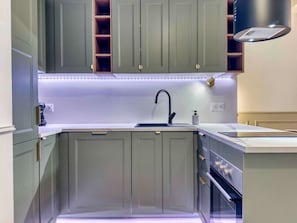 Une cuisine moderne dotée d’un évier encastré, d’appareils électroménagers en acier inoxydable et d’un éclairage sous les meubles hauts.